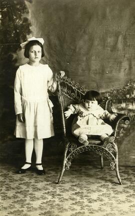Photographie d’une jeune fille debout et d’un enfant assis