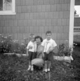 Femme avec deux enfants derrière une maison