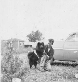 Un homme accroupi et son chien noir près d’une voiture