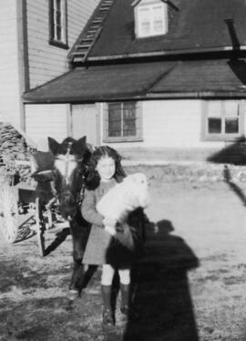 Une fillette, un chien et un cheval près d'une maison