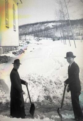 Un prêtre et un homme avec pelles près d'une église
