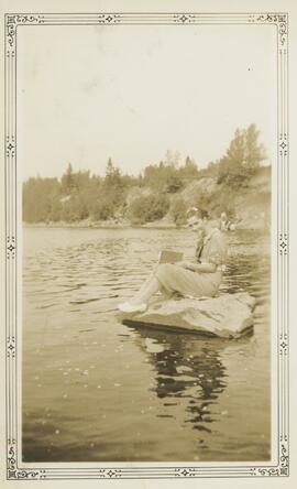 Femme assise sur un roche entourée d'eau qui lit un livre