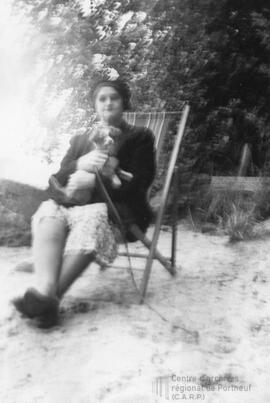 Femme assise sur une chaise à la plage avec un petit chien dans ses bras