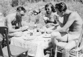Deux hommes et une femme en maillot de bain mangeant dehors à la table