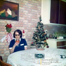 Une femme en train de boire à coté d’un mini sapin de Noël