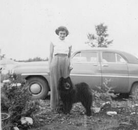 Une femme et un petit chien noir devant une voiture