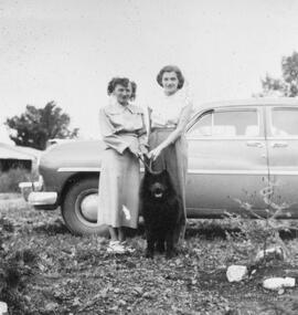 Deux femmes et un chien en laisse devant une voiture