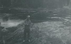 Homme sur un rocher près de l'eau tenant un appareil photo dans ses mains