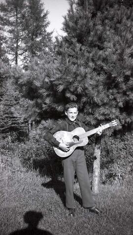 Vachon Roger avec sa guitare devant un pin