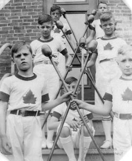 Sept enfants portant un chandail du Canada et tenant des bâtons en bois