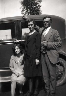 Une femme inconnue assise sur un marchepied d'une voiture avec un homme et une femme inconnues à côté