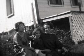 Deux jeunes femmes et une fillette assises dans l'herbe près d'une maison