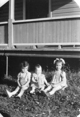 Photo de trois enfants assis dehors devant une maison