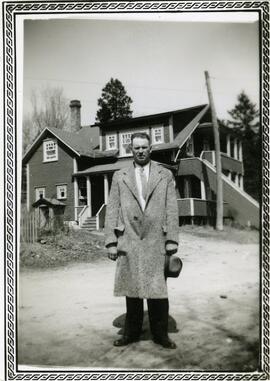 Un homme non identifié portant un long manteau devant une maison