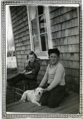 Deux enfants et un chien devant une maison