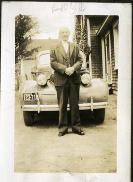 Un homme moustachu debout devant une voiture