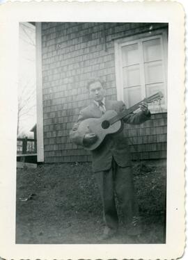 Malcolm Kingsborough tenant une guitare à l’extérieur d’une maison