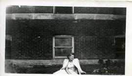 Mildred Parsons assise au sol devant un bâtiment en brique